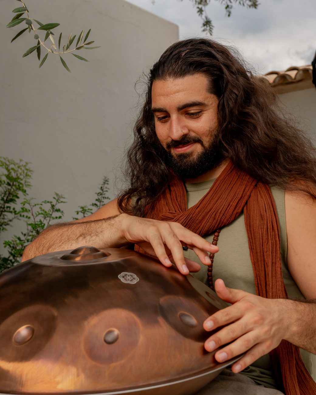 Emre playing a copper handpan, smiling down at the notes